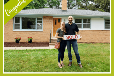 couple smiling outside of a house holding a sold sign