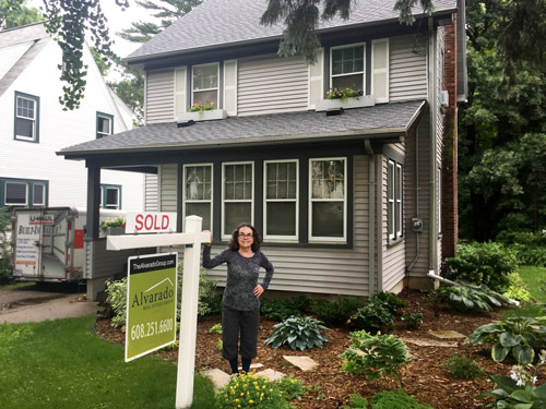 Woman outside of a grey and black house with a sold sign