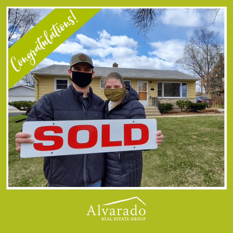 Couple smiling outside house holding a sold sign