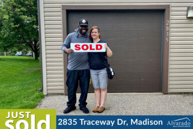 Couple smiling outside their home with a sold sign